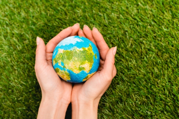 Cropped view of globe in female hands on green background depicting cleaner planet