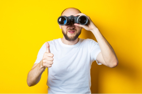 man looking through a binocular while doing a thumbs up depicting what to look for in a heating oil company