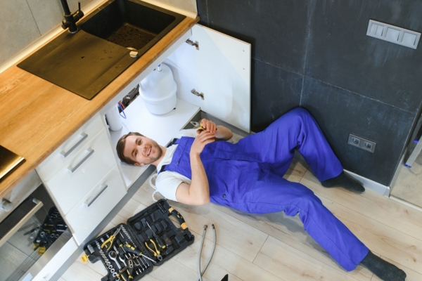 plumber checking under kitchen sink for faucet water pressure