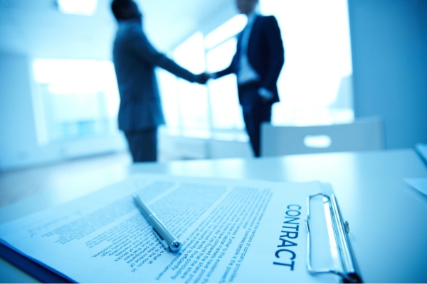 two men in the background shaking hands with contract on the table
