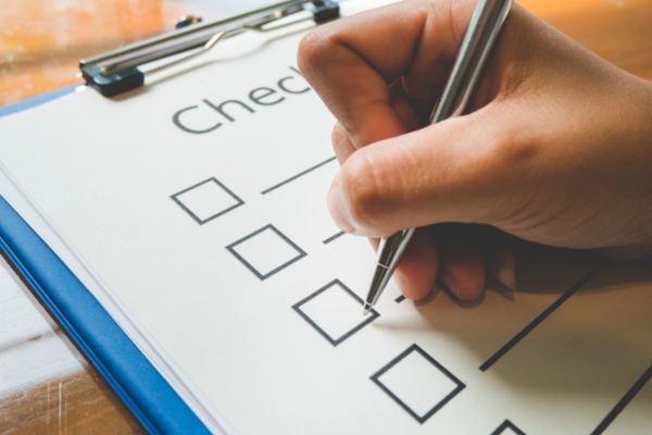 Close- up hand holding pen on check list paper depicting Key Factors When Selecting a Local Heating Oil Provider