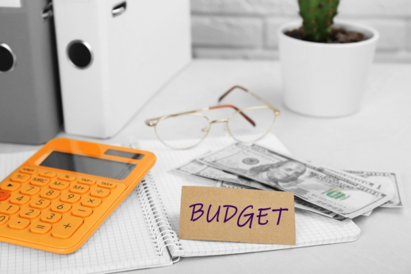 budget written on a brown card on top of a notebook beside cash and glasses depicting Heating Oil Expenses